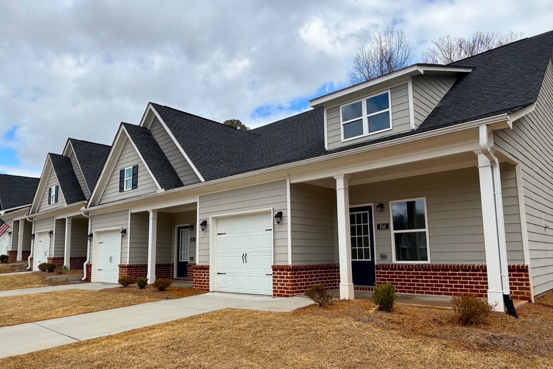 Row of new beige townhouses with white trim, garages, and a cloudy sky above