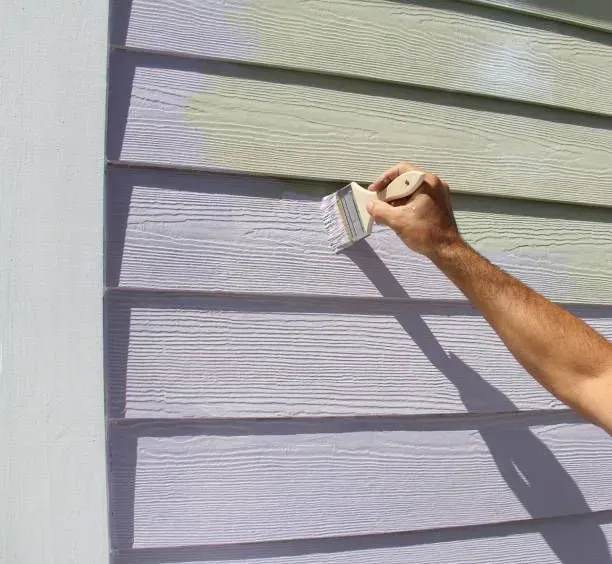 A person is painting the side of a house with a brush.