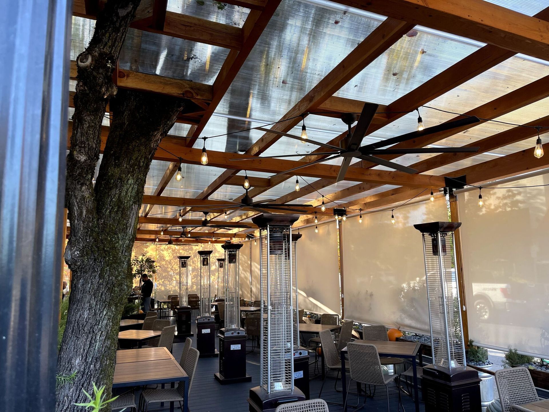 A restaurant with tables and chairs under a canopy with heaters.