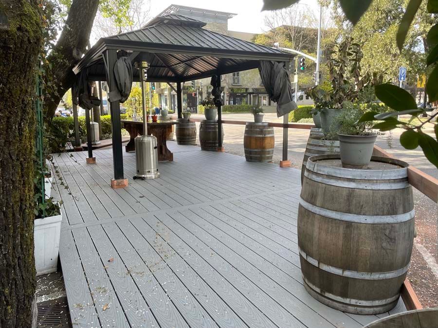 A wooden deck with barrels and a gazebo in the background.