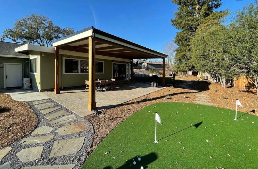 A house with a covered patio and a putting green in front of it.