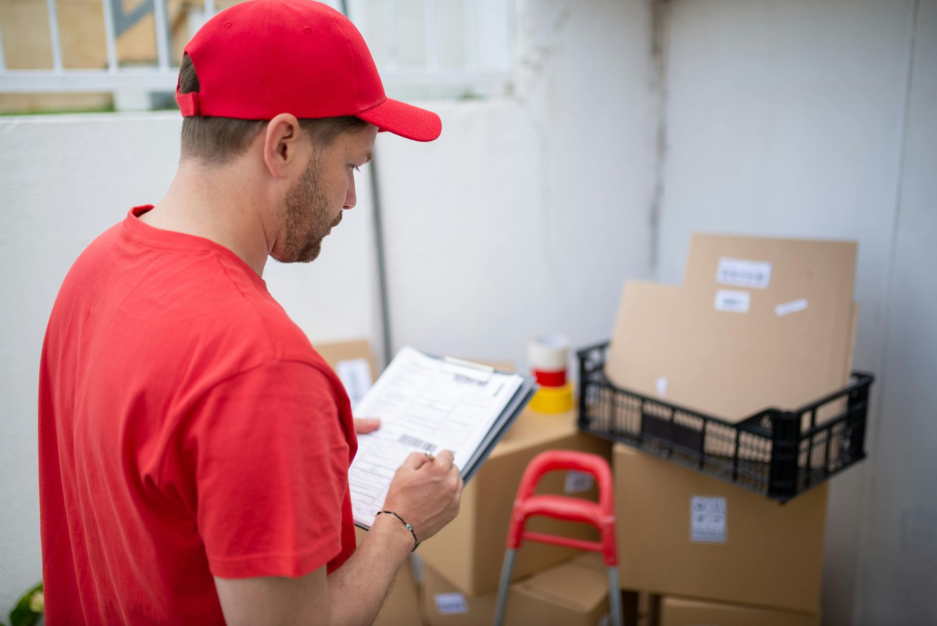 A delivery man is writing on a clipboard in front of boxes.
