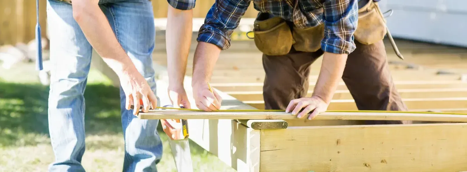 A man and a woman are measuring a piece of wood.