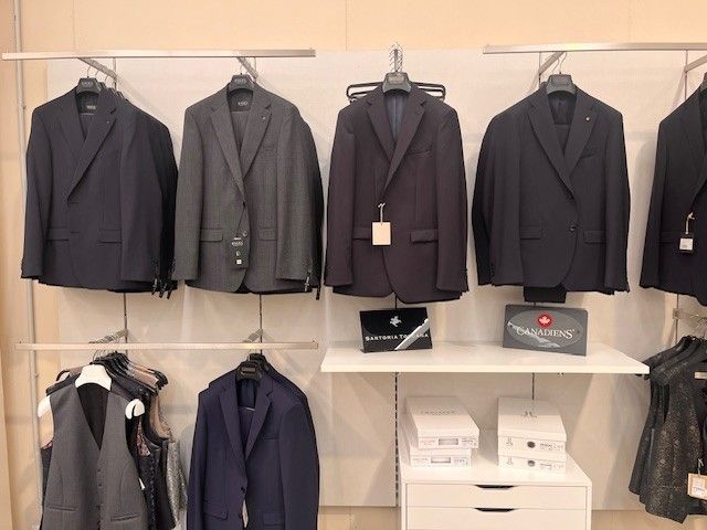 Abiti appesi in un negozio; giacche blu scuro, grigie e nere.
