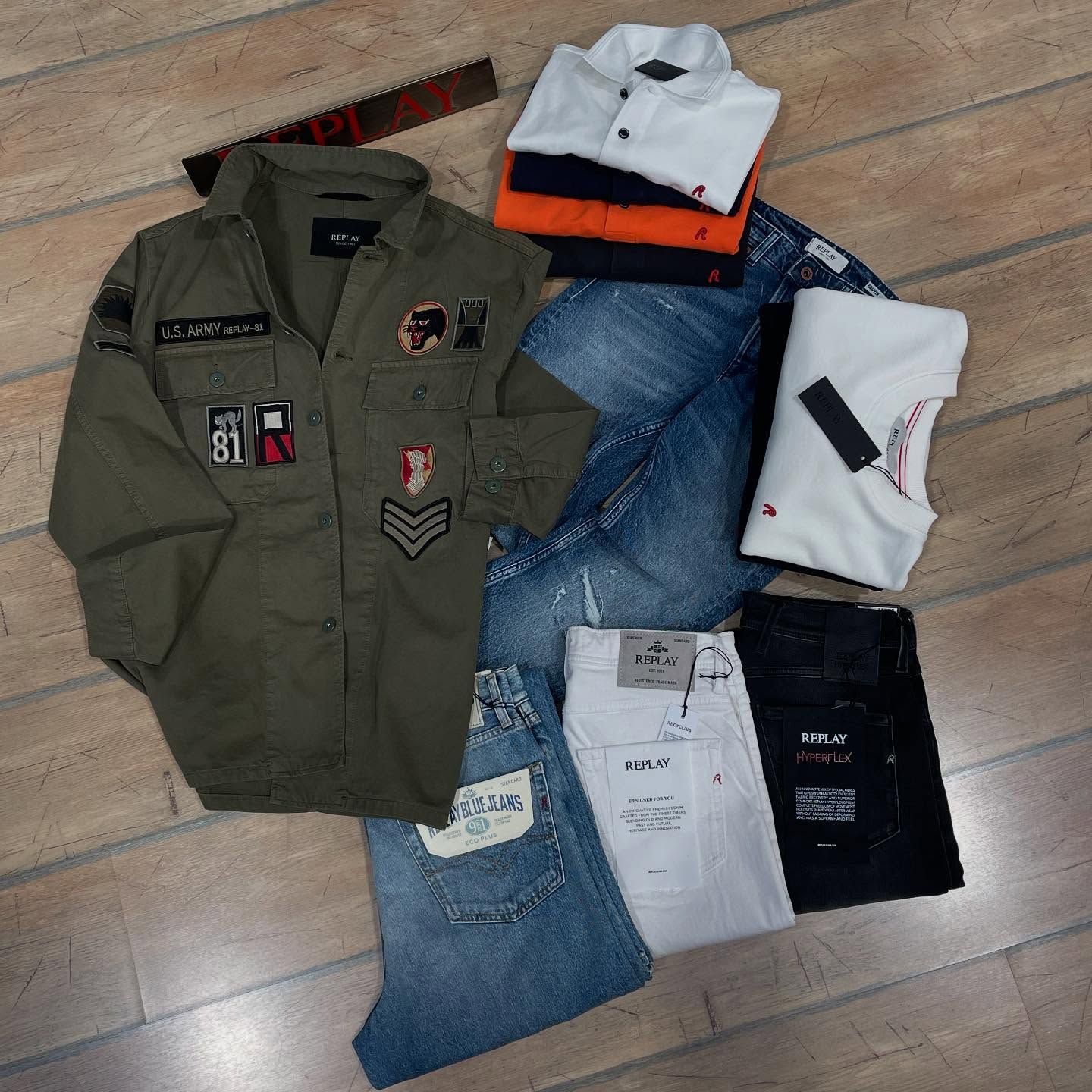 Abbigliamento maschile: giacca, jeans, polo di vari colori (verde, blu, bianco, arancione) su legno.