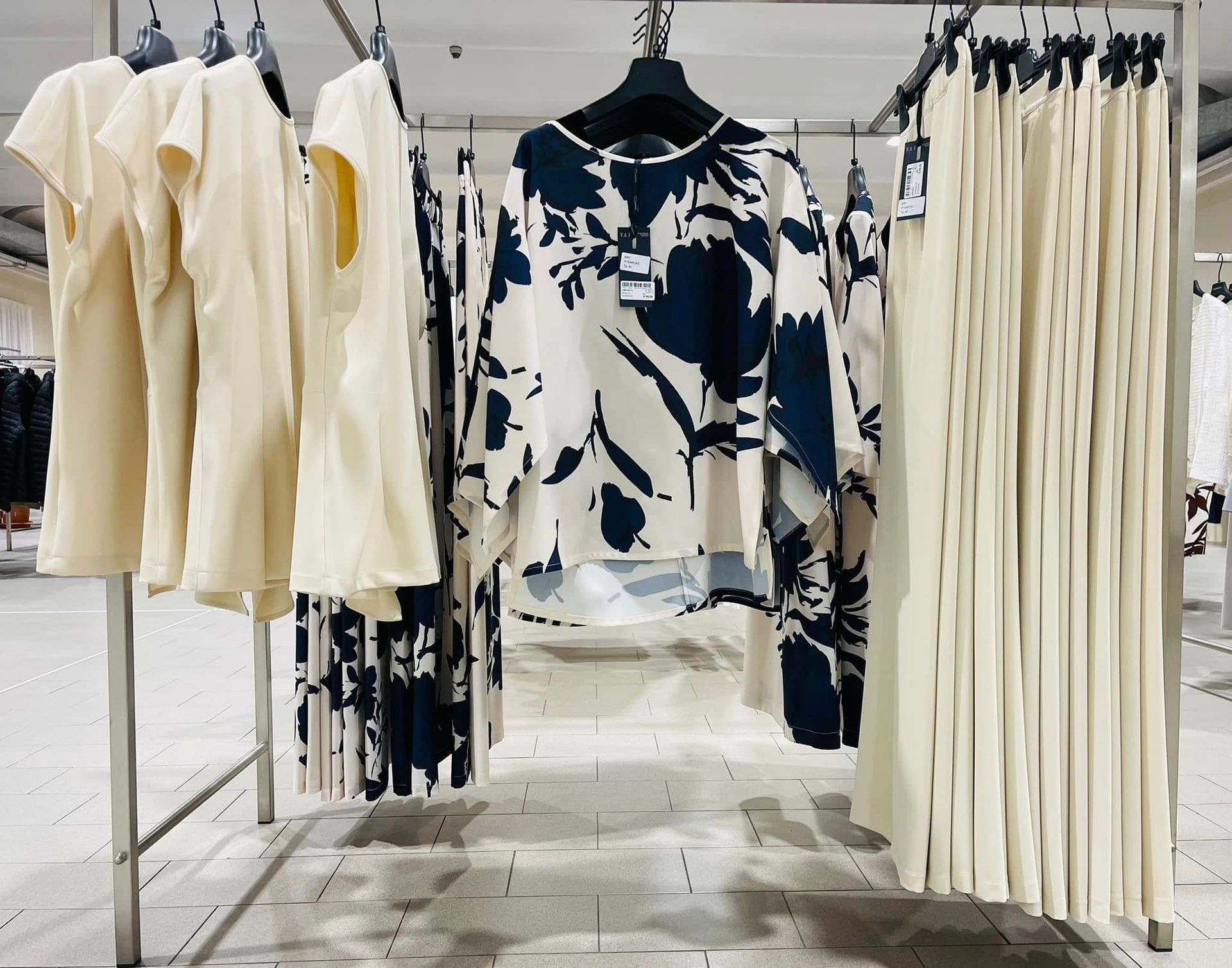 Appendiabiti con abiti dai toni neutri e camicette a fantasia. Interno del negozio ben illuminato.