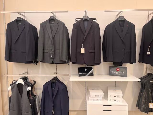 Abiti appesi su un espositore in un negozio. Vari colori scuri: blu navy, grigio e nero.