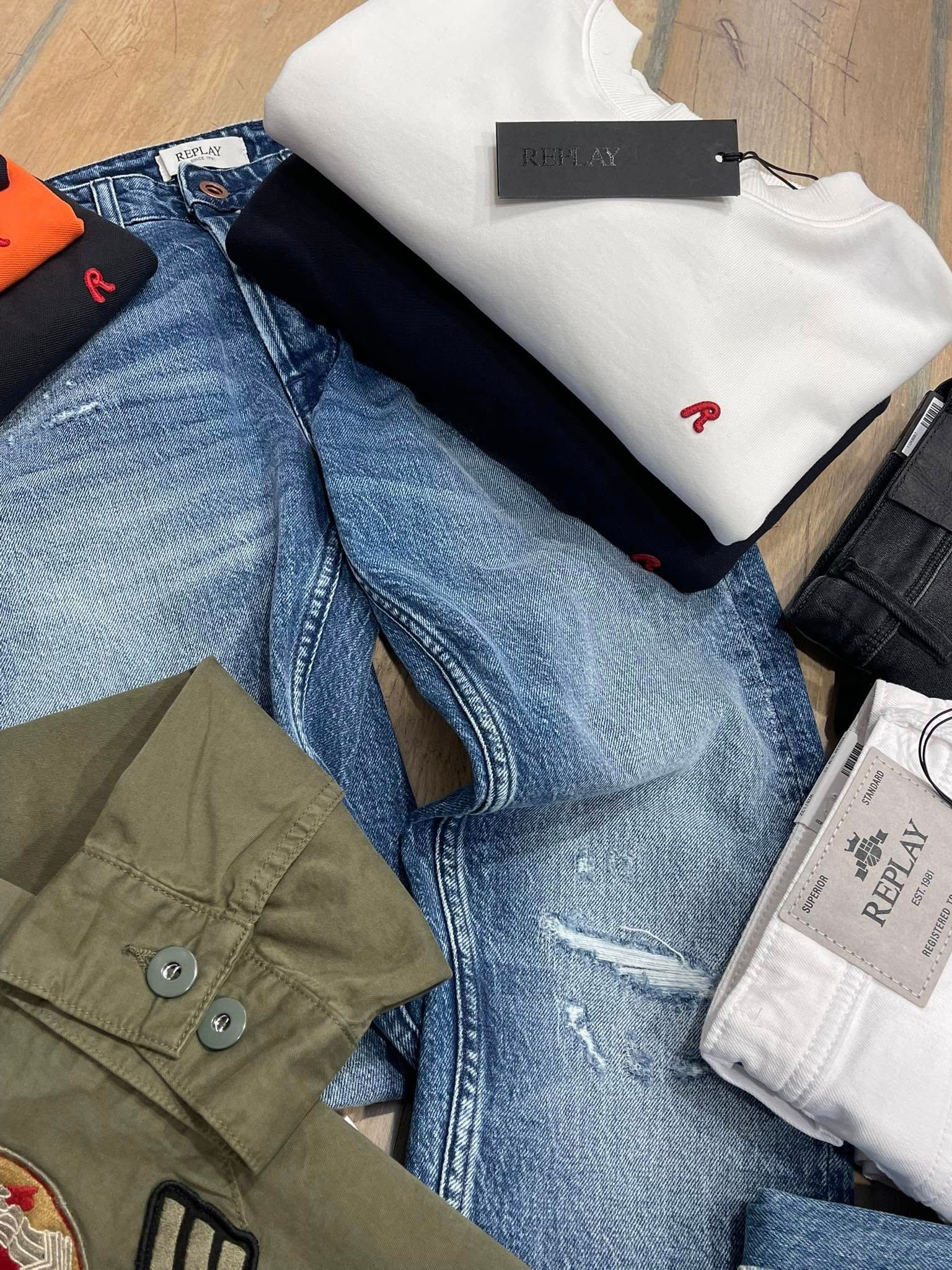 Assortimento di indumenti piegati, tra cui jeans, camicie e una giacca di vari colori, disposti su una superficie di legno.