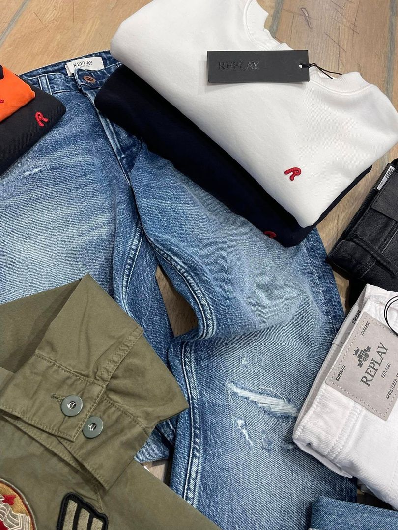 Assortimento di indumenti piegati, tra cui jeans, camicie e maglioni di vari colori, disposti su una superficie di legno.