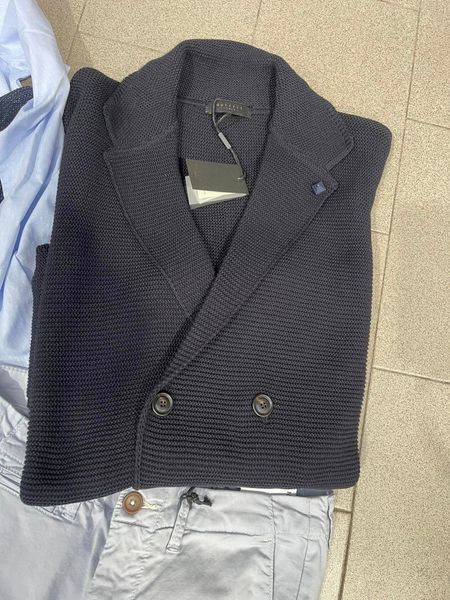 Blazer in maglia blu navy con bottoni e revers, sopra pantaloni azzurri piegati.