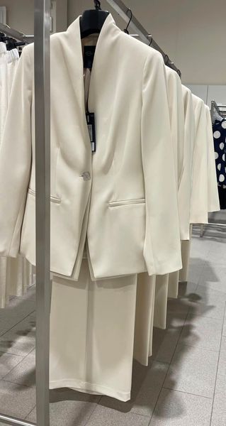 Un tailleur pantalone bianco sporco su uno scaffale di vestiti in un negozio.