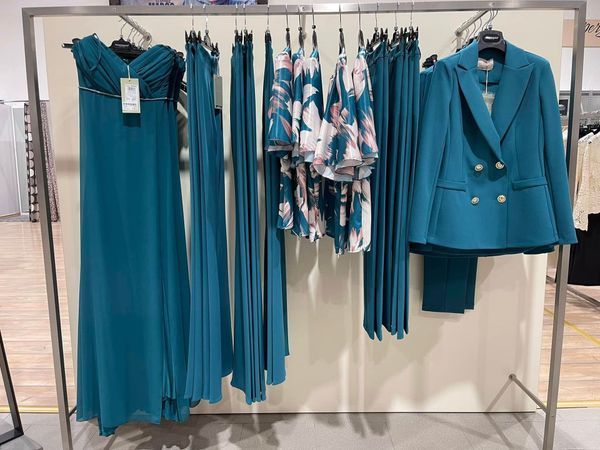 Espositore con abito verde acqua, pantaloni, top floreale e tailleur in un negozio.