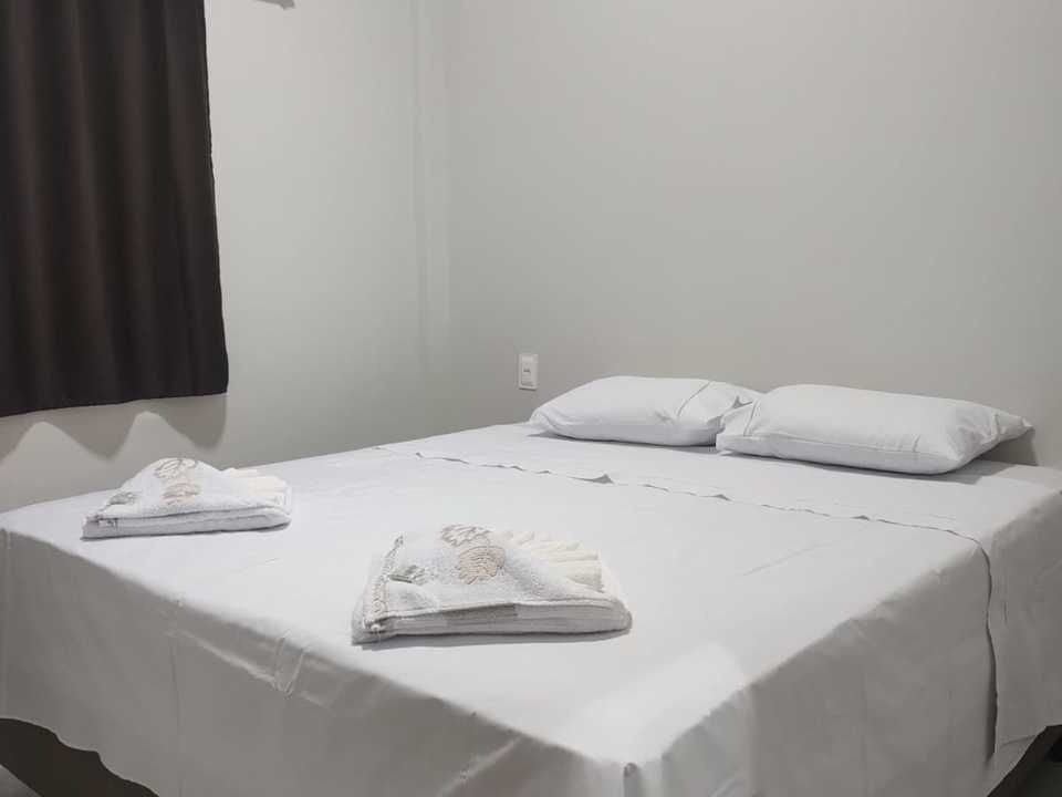 Um quarto com uma cama coberta com lençóis brancos, dois travesseiros e toalhas dobradas.