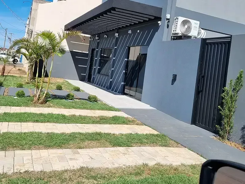 Prédio moderno com fachada cinza-escura, toldo e passarela ao lado de um gramado listrado.