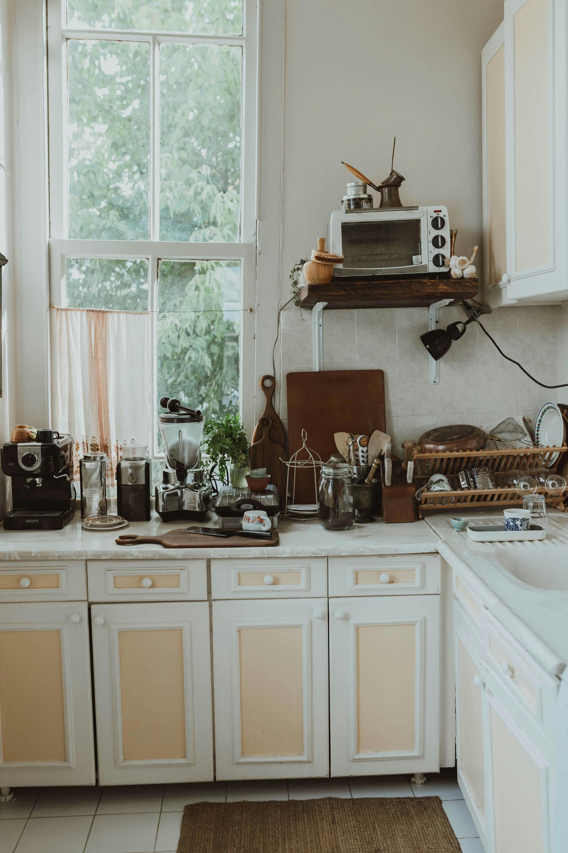 A kitchen with white cabinets , a sink , a microwave and a window.