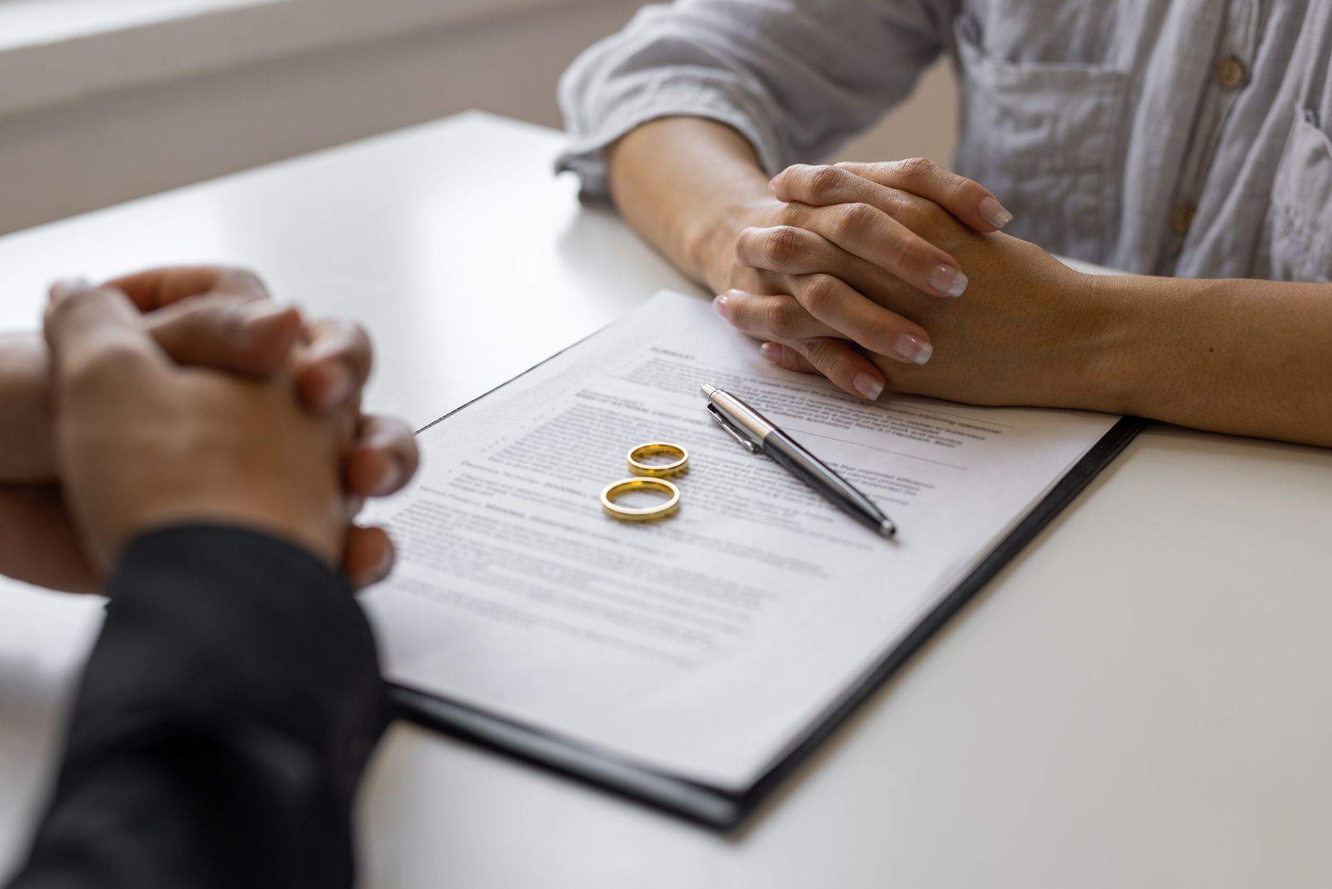Divorce attorney meeting with couple, contract and wedding rings on table