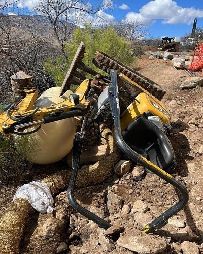 An overturned mini digger lies against a propane tank