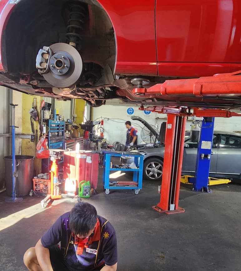 A Man is Working Under a Red Car in a Garage — JDM Mechanical & Aircon Repairs In Coconut Grove, NT