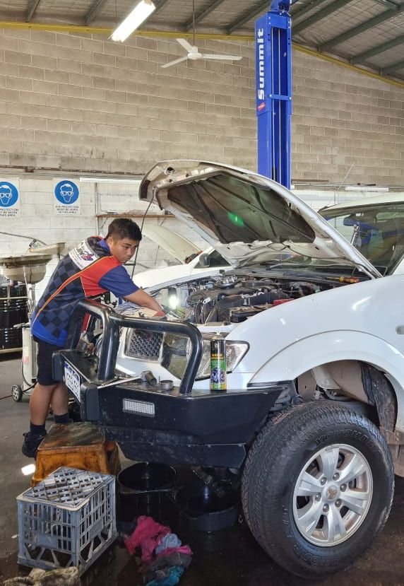A Young Boy is Working on the Engine of a White Truck in a Garage — JDM Mechanical & Aircon Repairs In Coconut Grove, NT