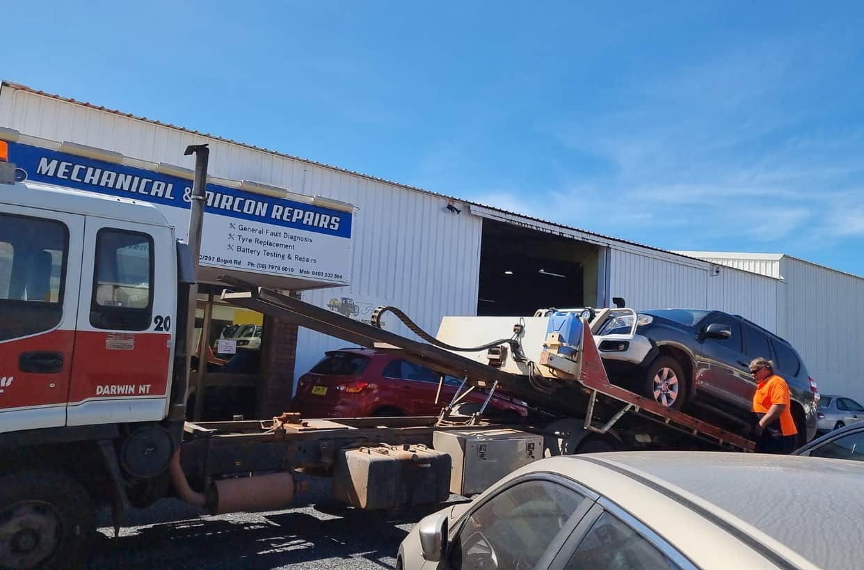 A Car is Being Towed by a Tow Truck in Front of a Building — JDM Mechanical & Aircon Repairs In Coconut Grove, NT