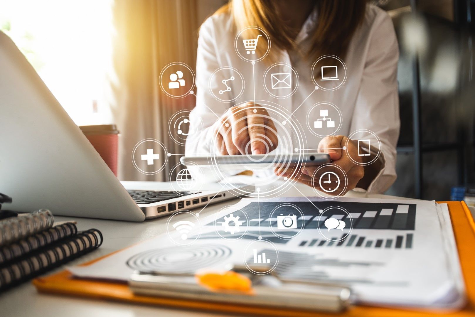 Woman in white shirt working on laptop and tablet, surrounded by digital icons and financial charts.