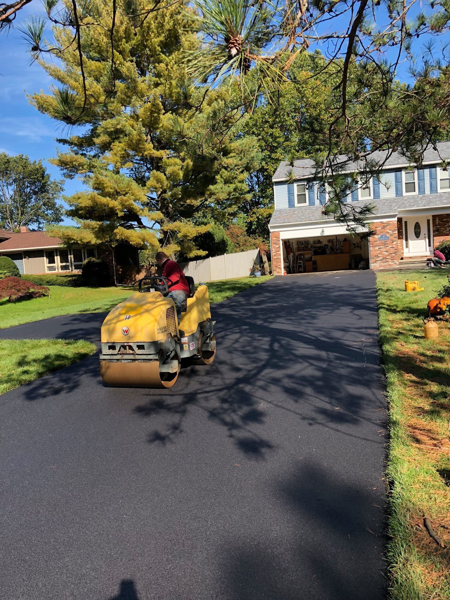 Asphalt roller compacting a newly paved driveway in front of a house.