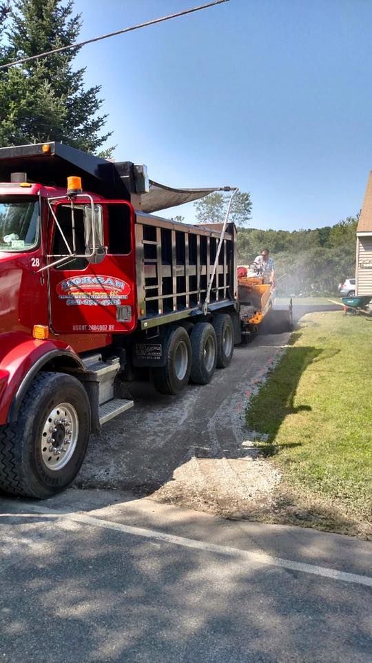 Red dump truck next to road paving machine on a sunny day.