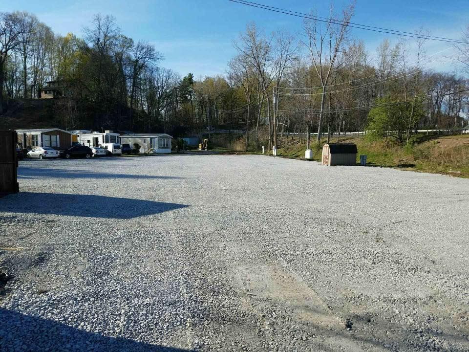 Gravel parking lot with mobile homes in background, trees and blue sky.