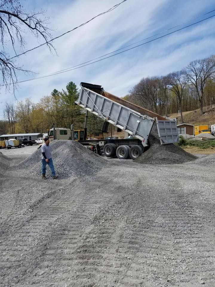 Dump truck unloading gravel at a construction site; man watches.