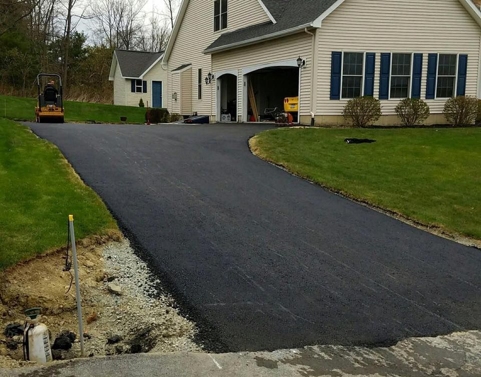 Newly paved asphalt driveway leading up to a beige house with a garage and green lawn.