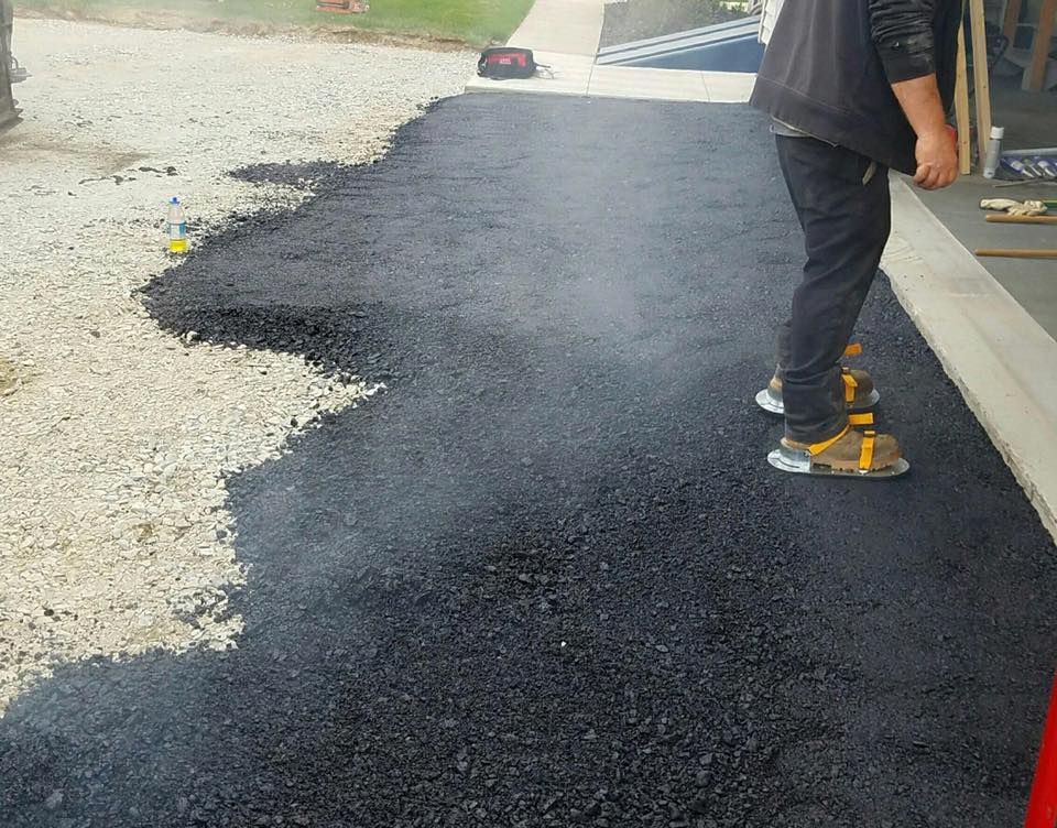 Person standing on newly paved asphalt, gravel driveway, construction site.