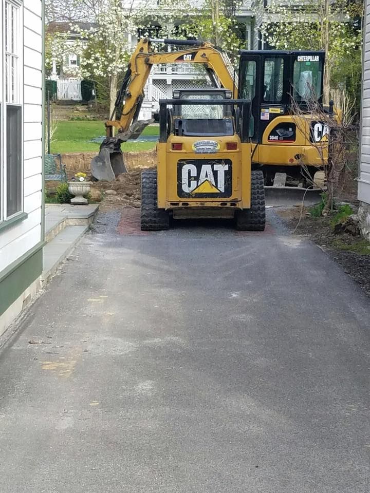 Yellow CAT skid steer and excavator on a paved driveway, likely for construction or landscaping work.