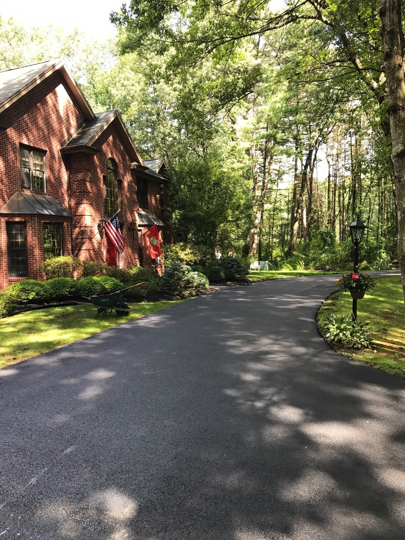 Brick house with long driveway, surrounded by trees. American flag displayed.