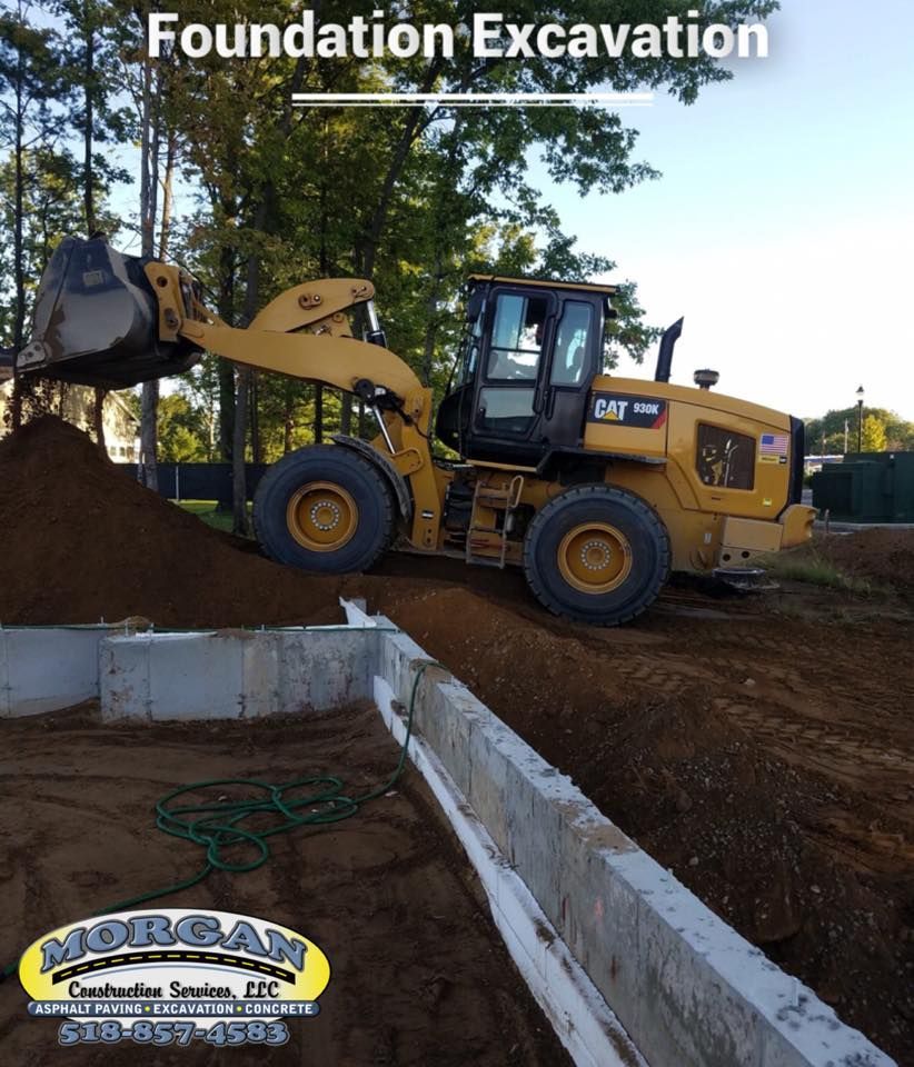 Yellow front-end loader excavating dirt next to a concrete foundation. 