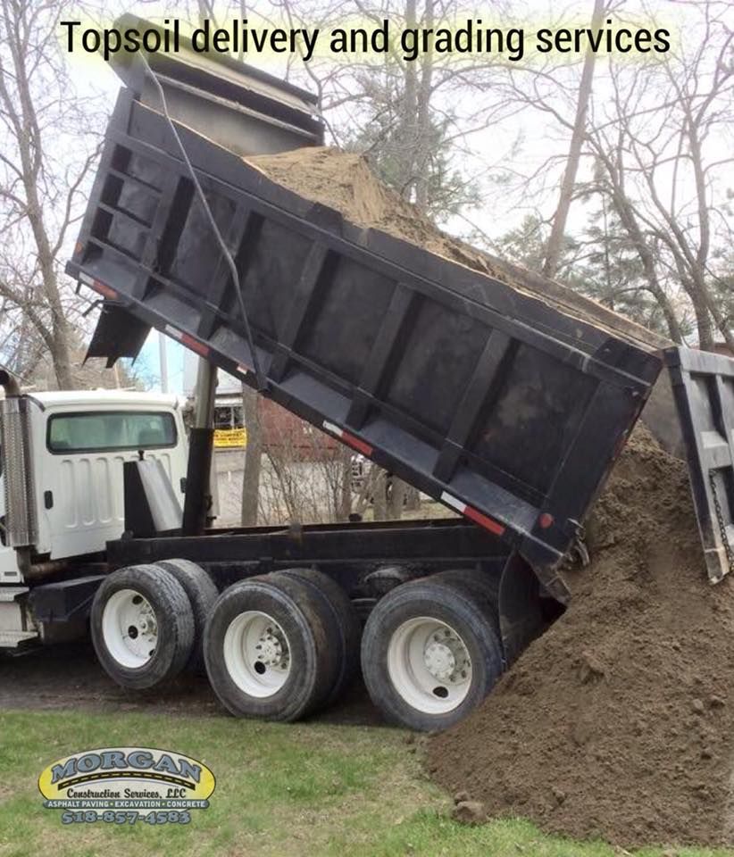 Dump truck unloading topsoil on grass.