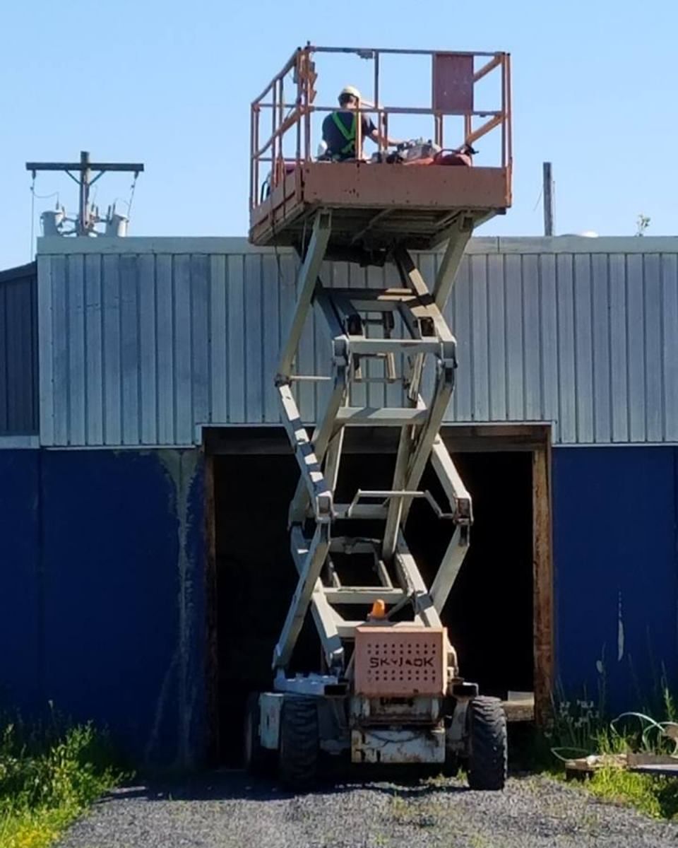 Worker on scissor lift near blue building with open doorway.