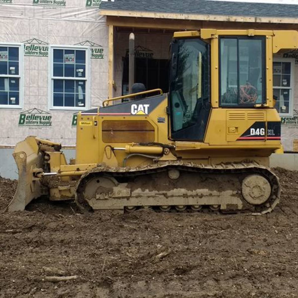 Yellow Caterpillar D4G bulldozer on muddy ground, near a building under construction.