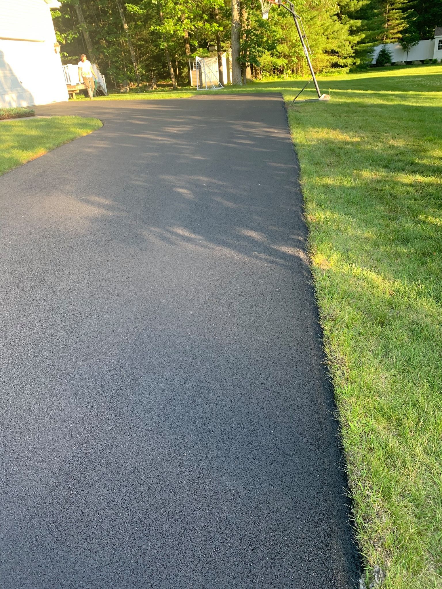 Newly paved black asphalt driveway next to a strip of green grass and a white building.
