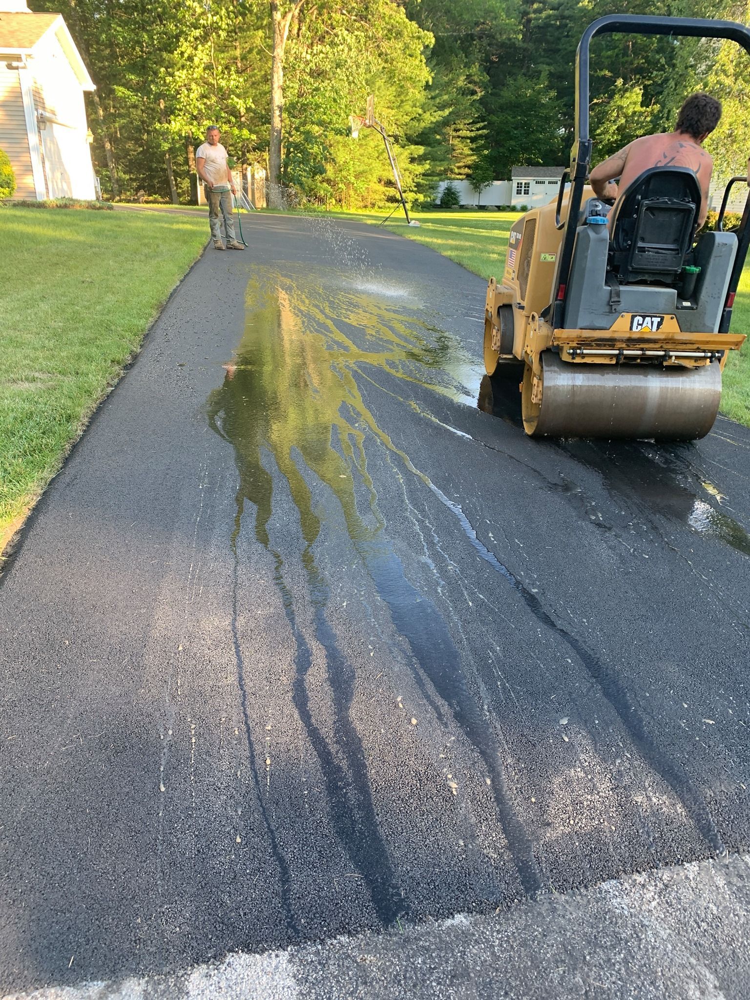 Paving a driveway: a worker operates a roller compactor while another spreads the asphalt.