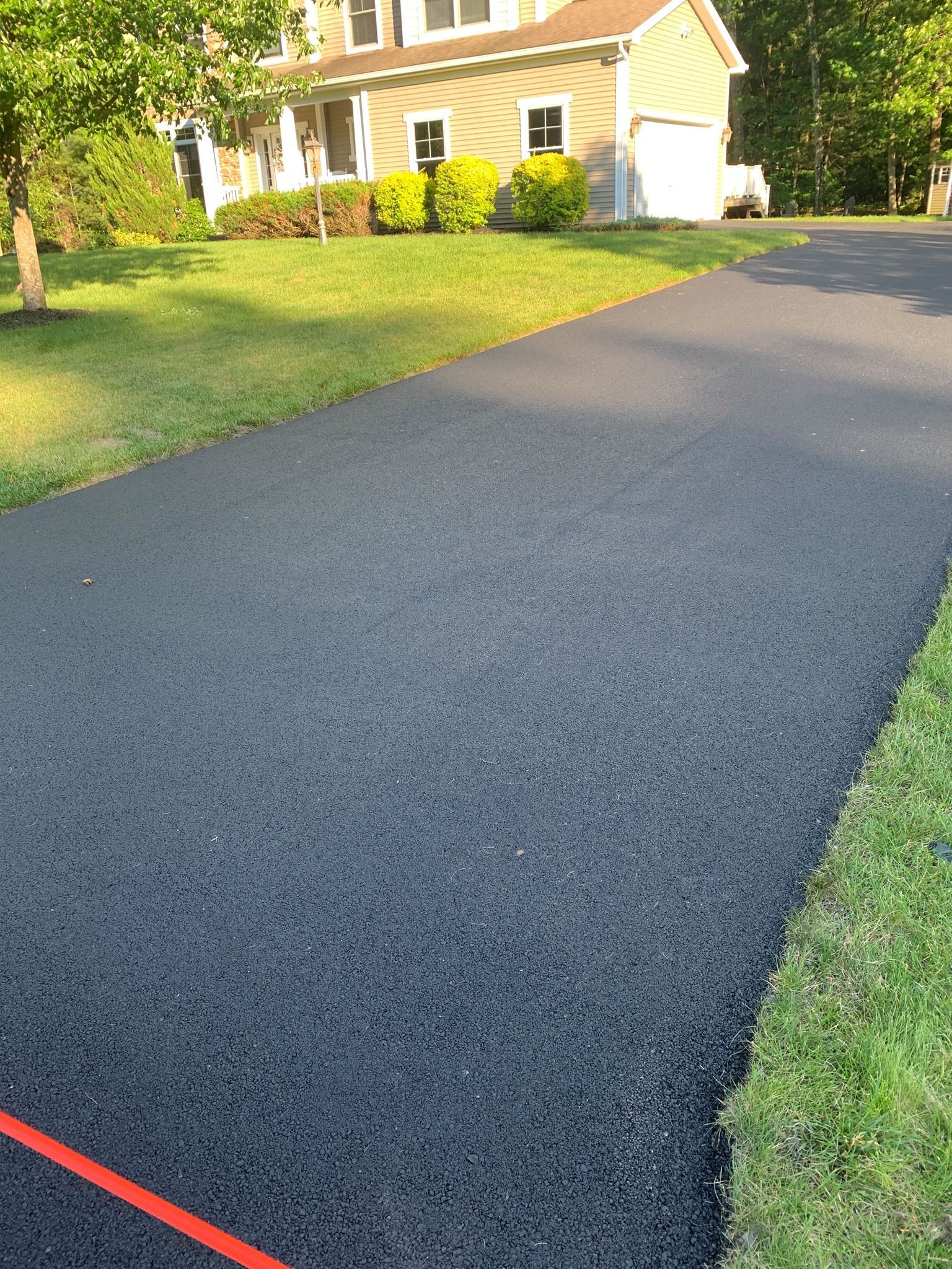 Freshly paved asphalt driveway leading to a house, with green lawn on either side.