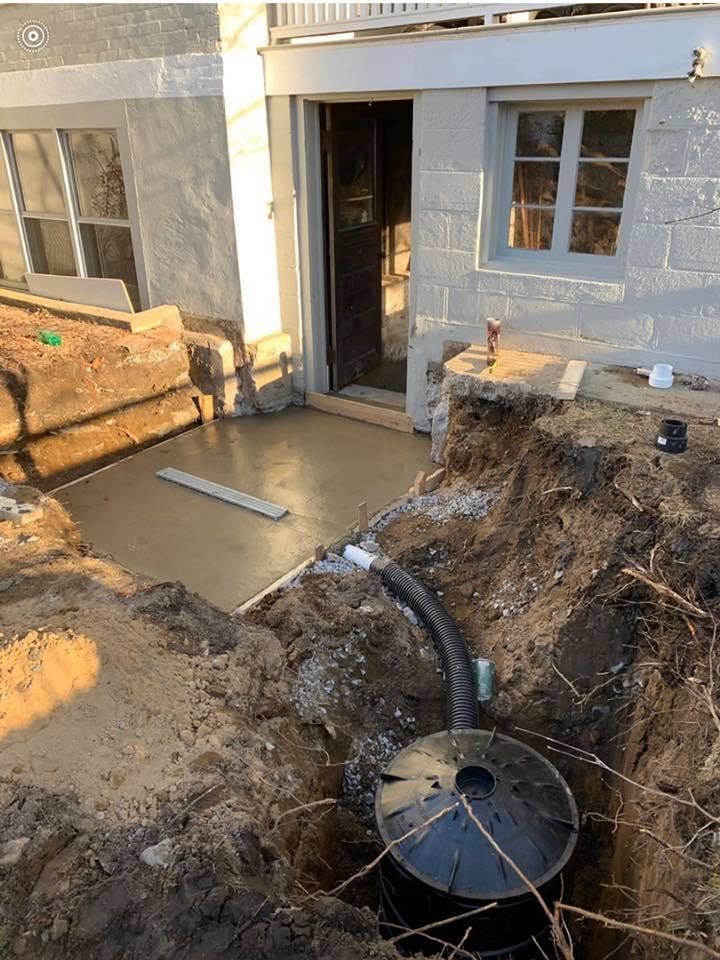 Exterior view: Concrete patio under construction, with a drain system in a trench.