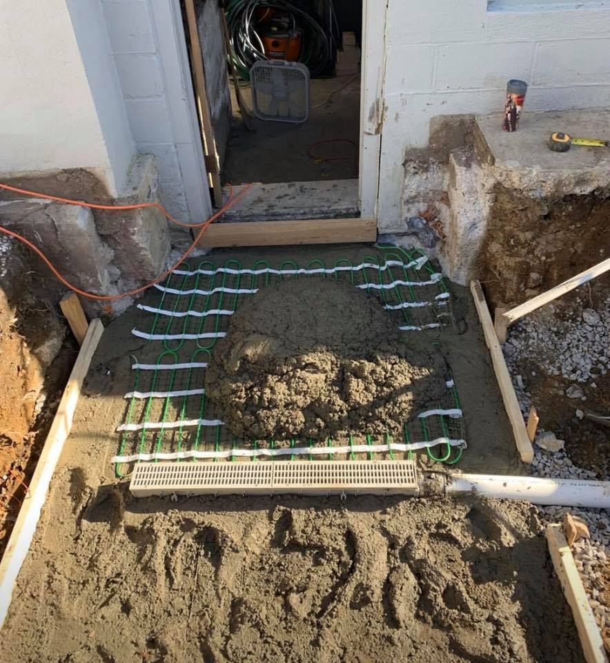 Wet concrete poured over a green heating mat in a doorway, surrounded by wooden framing and a trench.