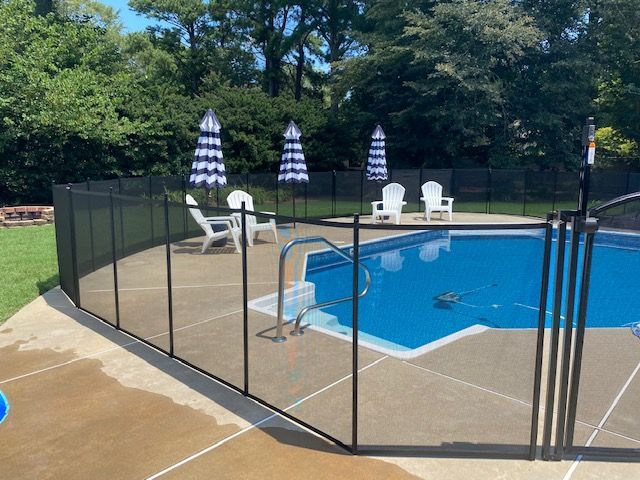 A fence around a swimming pool with chairs and umbrellas