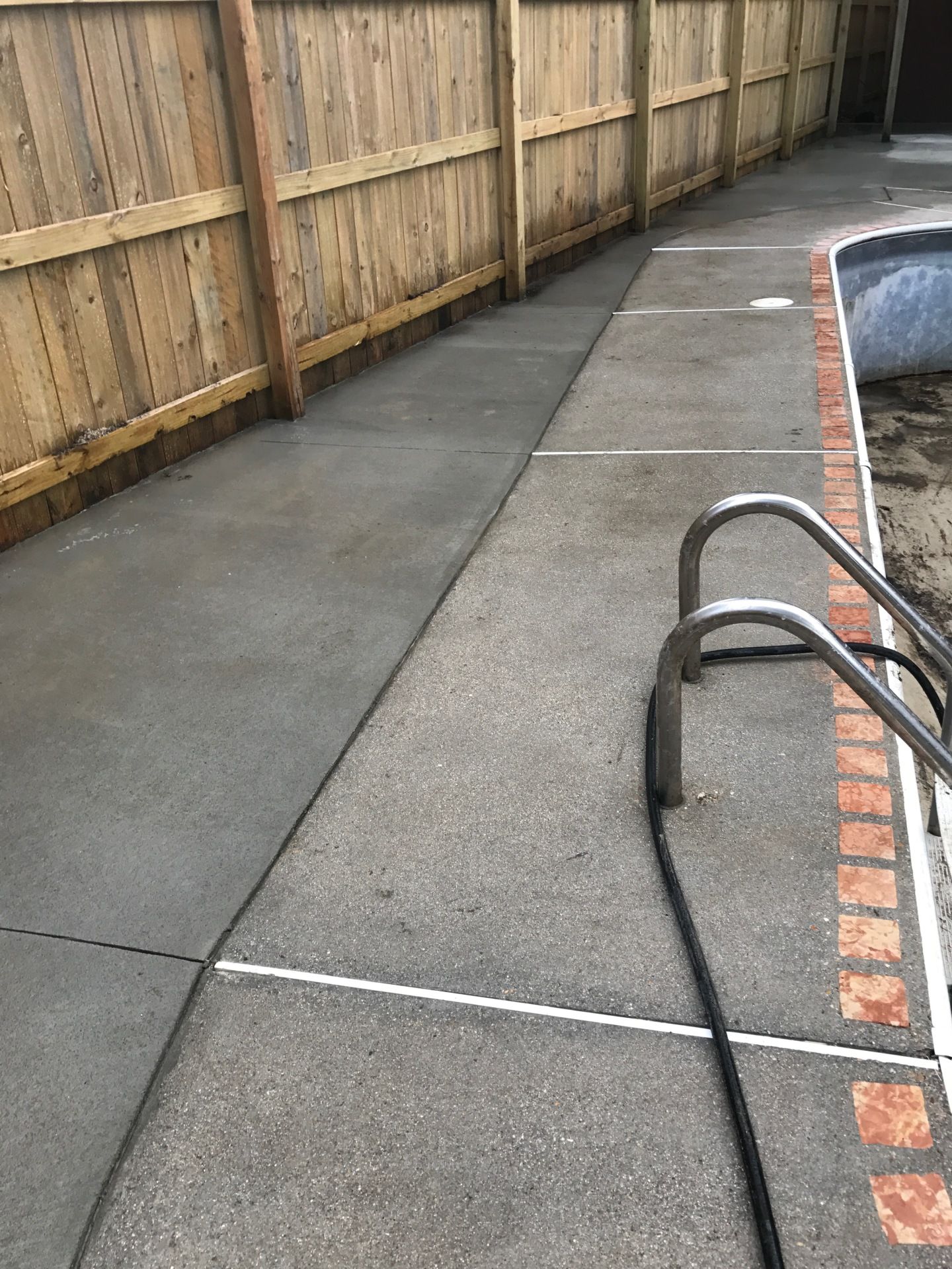 A concrete walkway next to a swimming pool with a wooden fence.