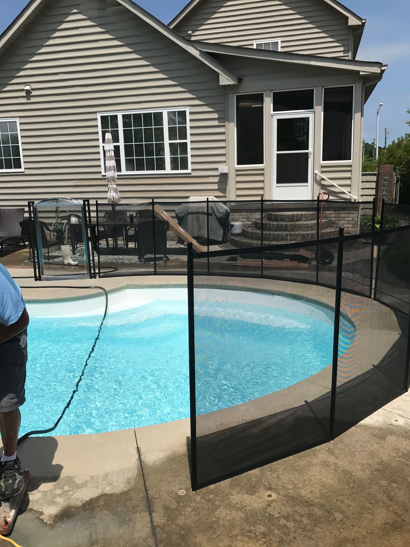 A man is standing next to a swimming pool in front of a house.
