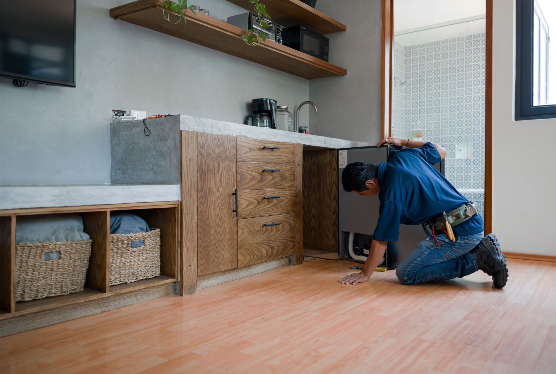 A man is kneeling on the floor in a kitchen.