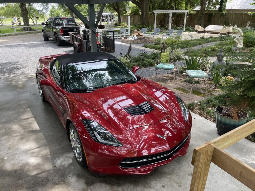 A red sports car is parked under a carport in a driveway.