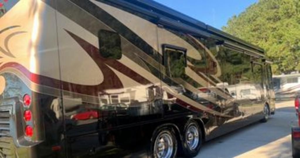 A large rv is parked on the side of the road next to a car.