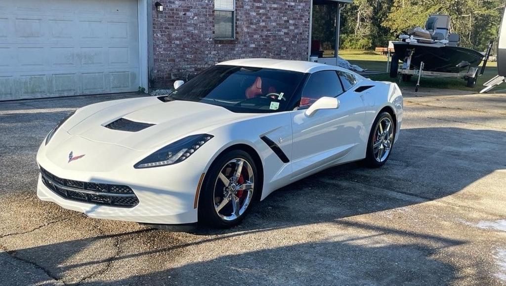 A white corvette is parked in front of a garage.