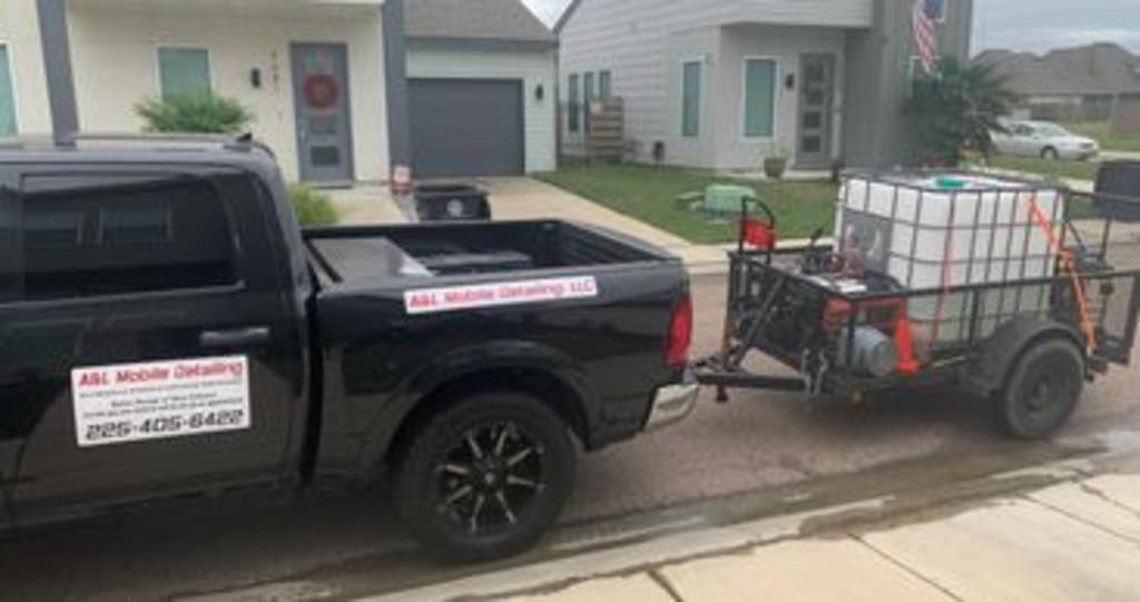 A black truck with a trailer attached to it is parked in front of a house.
